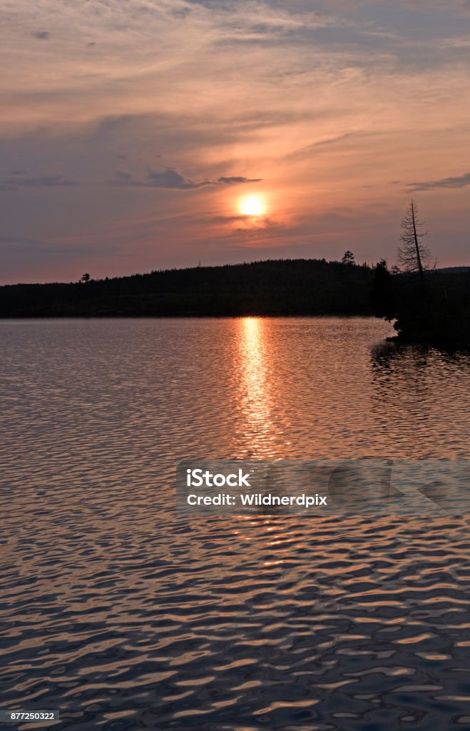 The Sun Setting Through Evening Clouds The Sun Setting Through Evening Clouds on Little Saganaga Lake in the Boundary Waters in Minnesota Beauty Stock Photo