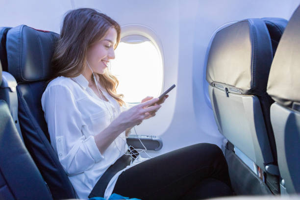 молодая женщина слушает музыку во время авиаперелетов - mobile phone seat belt text messaging smiling стоковые фото и изображения