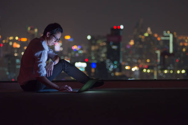 business-mann mit computer-laptop auf dem dach der stadt bei nacht - roof men business city stock-fotos und bilder