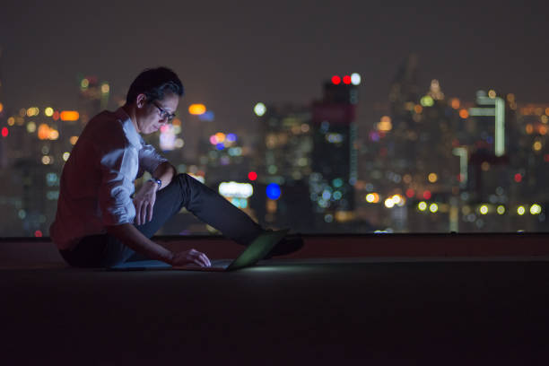 hombre de negocios con ordenador portátil en el techo de la ciudad en la noche - roof men business city fotografías e imágenes de stock