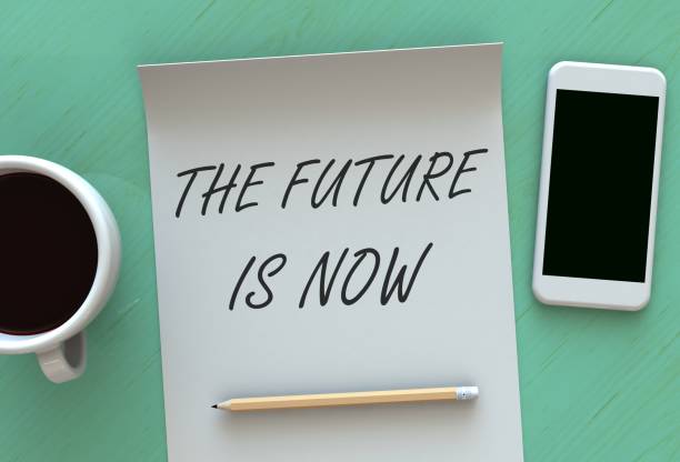 istock The Future is Now, message on paper, smart phone and coffee on table 877273960