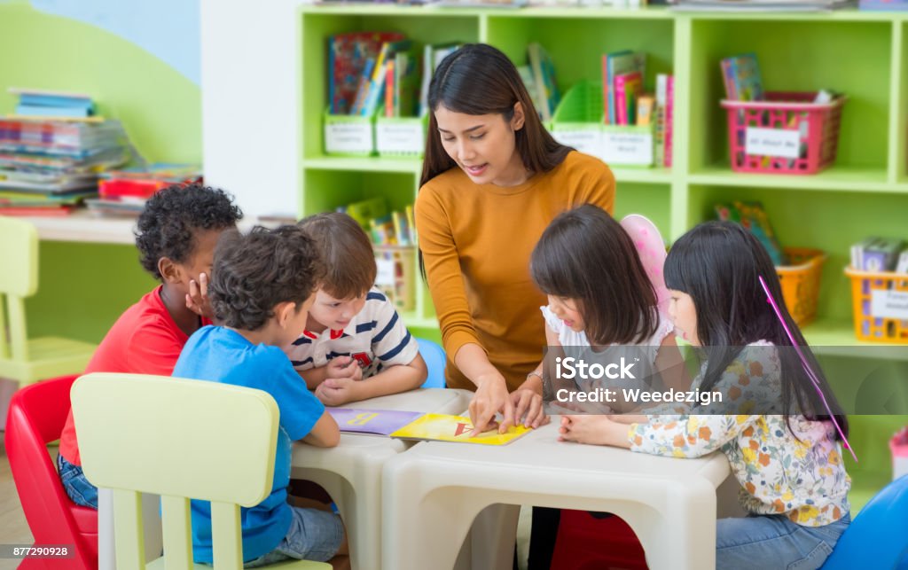 Asian female teacher teaching mixed race kids reading book in classroom,Kindergarten pre school concept. Asian female teacher teaching mixed race kids reading book in classroom,Kindergarten pre school concept Teacher Stock Photo