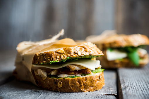 Sandwich with cereal bread, chicken, pesto and cheese on the rustic wooden background. Selective focus. Shallow depth of field.