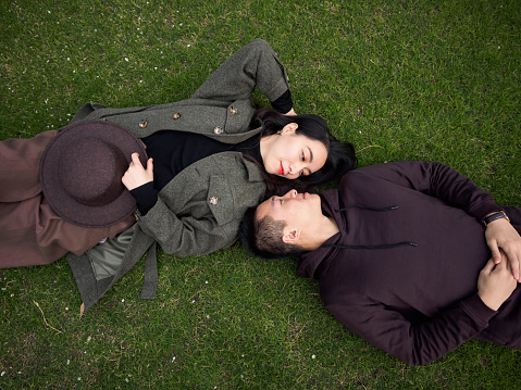 High angle view of couple of Chinese young people lying on green grass field and looking each other full of love, lover concept.