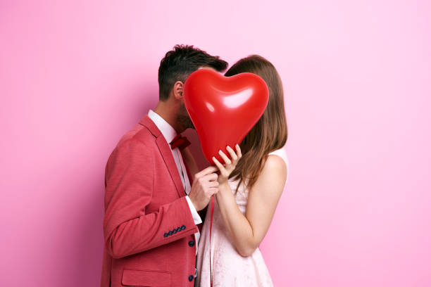 Affectionate couple covering face with balloon and kissing stock photo