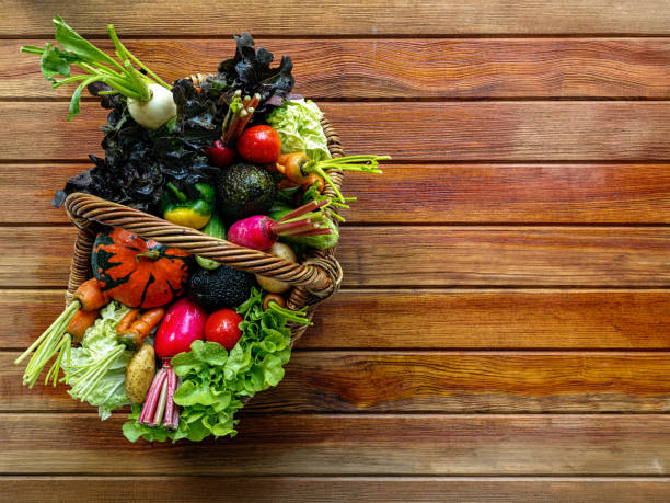 istock Fresh salad vegetables in a thick wicker basket on a wood panel table background. 877321566
