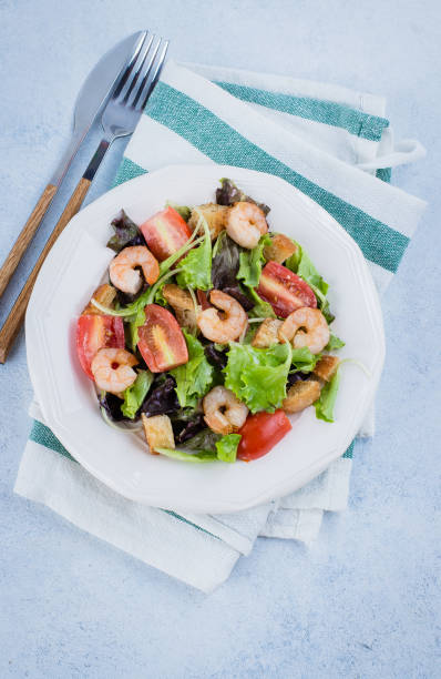 istock Fresh caesar salad on white plate with lettuce, cherry, parmesan cheese and shrimps on stone table background. Healhty Food Snack Concept. Top view Copy Space 877324896
