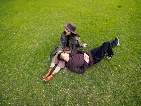 High angle view of a Chinese woman sit on green grass field and her boyfriend sleep on her knees, lover concept.