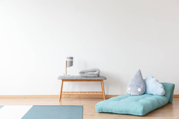 Kid's room with blue mattress Grey pillow on blue mattress next to wooden stool with lamp in kid's room with carpet and empty white wall carpet cushion stock pictures, royalty-free photos & images