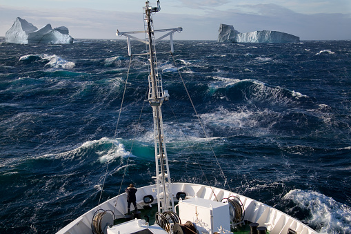A ship rolling in heavy seas near icebergs in Scoresbysund on the east coast of Greenland.