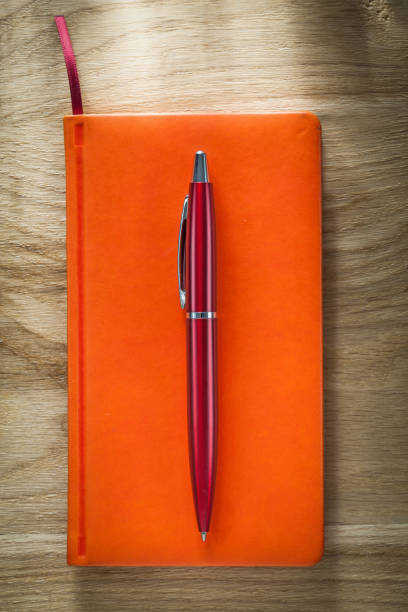istock Orange notebook pen on wooden board 877349628