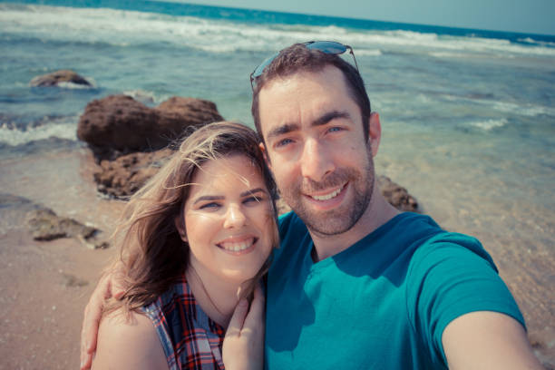 istock Young couple taking selfie with smartphone or camera at the beach 877349996