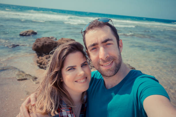 istock Young couple taking selfie with smartphone or camera at the beach 877350276