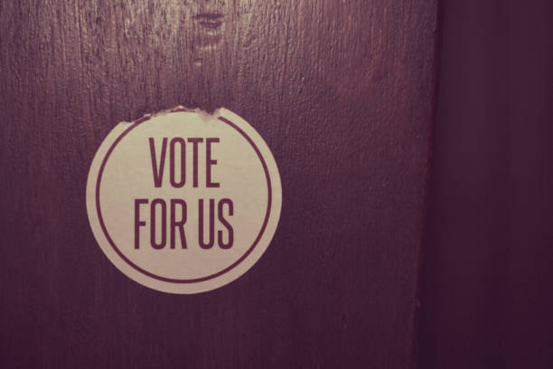 istock Peeling round sticker with the words Vote For US printed 877359362