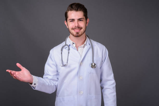 istock Young bearded handsome man doctor against gray background 877363924