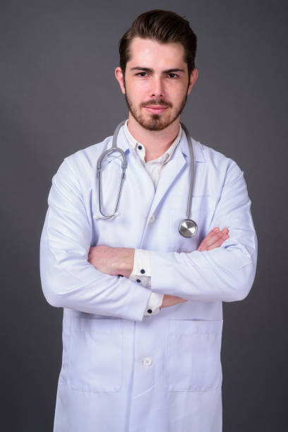 istock Young bearded handsome man doctor against gray background 877364008