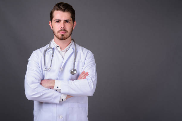 istock Young bearded handsome man doctor against gray background 877364148