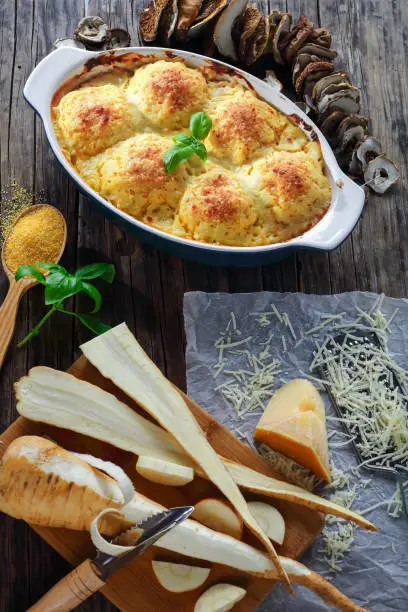 polenta vegetarian polpette stuffed with mushrooms ragout and baked in oven with parmesan cheese and parsnip sauce in baking dish. ingredients at background, vertical view from above