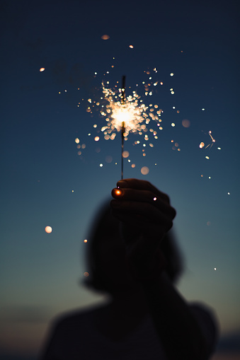 Close-up view of hand holding burning sparkler in evening darkness.