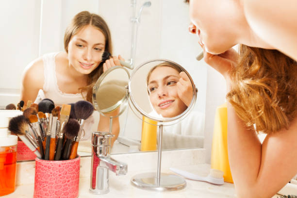 istock Young woman apply makeup, seen in bathroom mirror 877382218