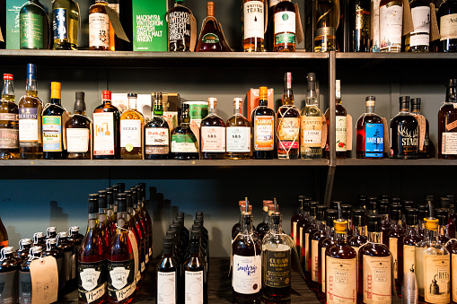 London, UK - 20 October, 2017: wide angle color image depicting a large selection of different bottles of rum and whisky on display at a liquor stall at Borough Market in London, UK - one of the oldest and most popular food and drink markets in the world. The shelves are staked full of the spirits, many of which are rare, luxurious and expensive.