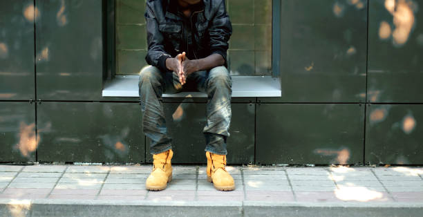 Street fashion concept, african man in black jacket, jeans and boots sitting in the city stock photo