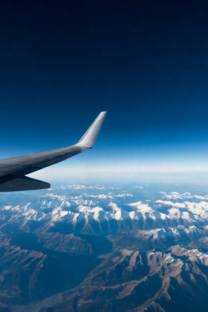 istock Wing of plane flying over clouds and mountains. 877446076