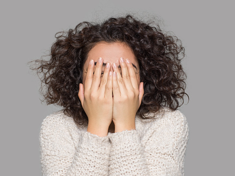 Young woman covering eyes with hands, studio shot