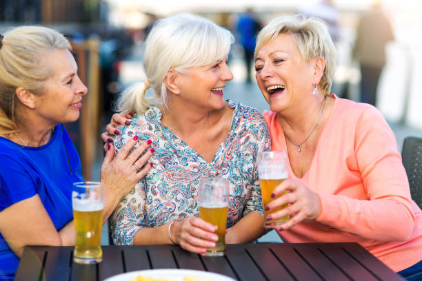 donne anziane sorridenti che bevano una birra in un pub all'aperto - friendship drinking beer group of people foto e immagini stock