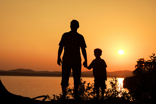 father and son playing on the coast of lake in the mountains of at the sunset timefather and son playing on the coast of lake in the mountains of at the sunset time