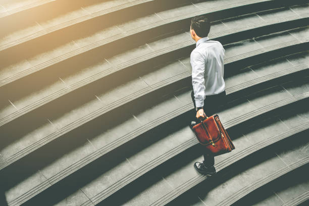 istock Young Asian businessman holding Brown leather bag  working on  staircase go office hurry work time with sunset top view and vintage tone 877570088