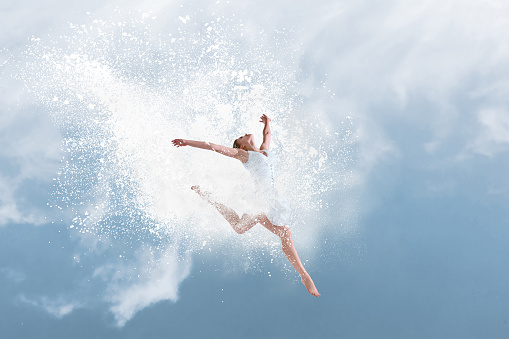Beautiful ballet dancer jumping inside cloud of powder in front of blue sky
