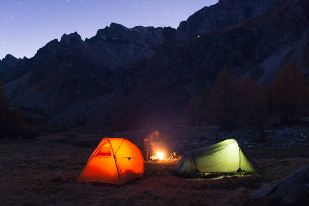 Photo of Friends camping under starry sky with two tents and campfire in blue hour at night