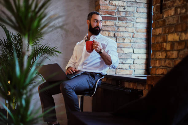 istock Urban bearded male drinks coffee and using a laptop. 877719414