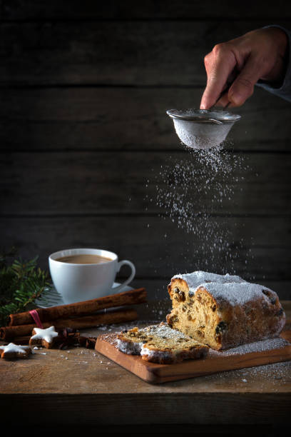 istock christmas cake, in germany christstollen is sprinkled with icing sugar, coffee cup, spices and cinnamon star cookies on a rustic wooden table, dark vintage background with copy space, vertical 877737264