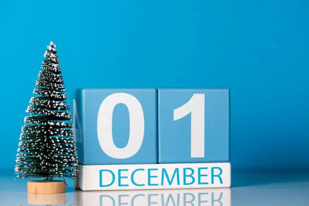 Photo of December 1st. Day 1 of december month, calendar with little christmas tree on blue background. Winter time. New year concept