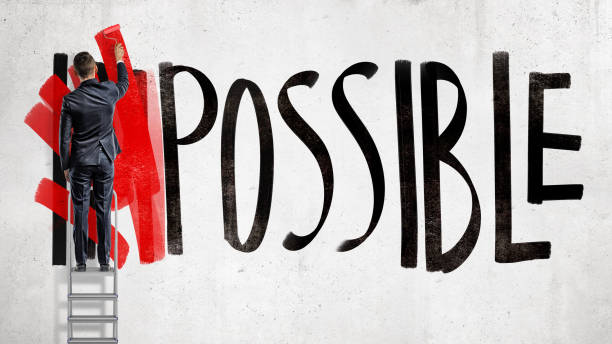 A businessman stands on a stepladder and hides the word Impossible written on the wall using a red paint roller. A businessman stands on a stepladder and hides the word Impossible written on the wall using a red paint roller. Business and success. Goals and planning. Impossible made possible. impossible possible stock pictures, royalty-free photos & images