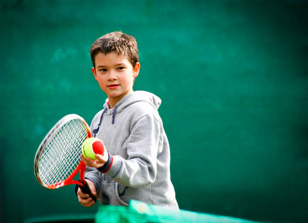 pequeño jugador de tenis en un fondo verde borroso - tennis child childhood sport fotografías e imágenes de stock