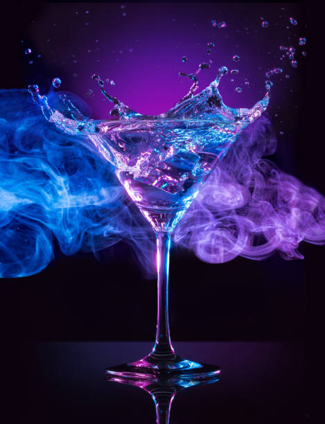 creating a signature drink martini cocktail splashing on smoky blue and purple background martini glass photos stock pictures, royalty-free photos & images