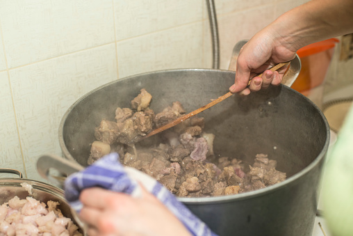 Preparation of pork meat for preservation closeup, stewing in a saucepan, mixing with a wooden spoon, homemade food