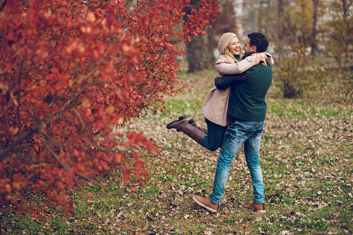 Young man holding his girlfriend in arms while they are having fun in the autumn park.