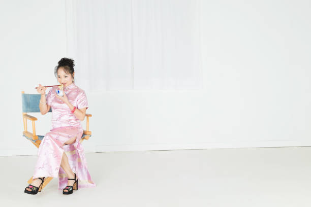 signora cinese che indossa un cheongsam rosa che mangia noodles. - cheongsam chinese culture indoors looking at camera foto e immagini stock