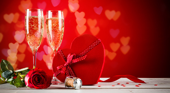 Background of Valentines day celebration with champagne, rose, heart shaped present and red candies.