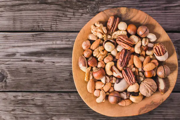 Plate of various fresh nuts on old rustic table top view with copy space