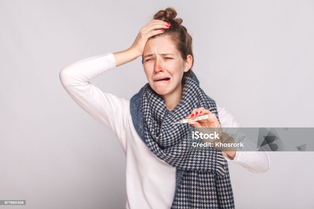 Unwell sick woman have temperature, holding head and cry. Unwell sick woman have temperature, holding head and cry. Studio shot, isolated on gray background Clown's Nose Stock Photo