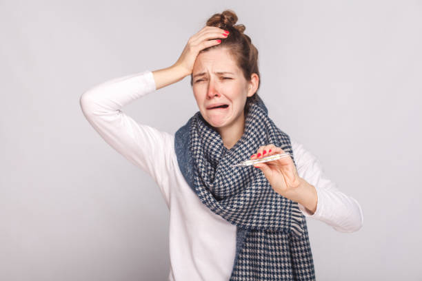 Unwell sick woman have temperature, holding head and cry. Unwell sick woman have temperature, holding head and cry. Studio shot, isolated on gray background clown's nose stock pictures, royalty-free photos & images