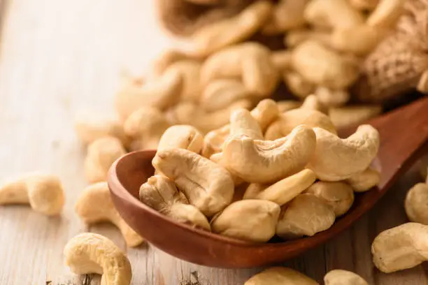 Photo of close up of cashew nuts in wood spoon on wood table