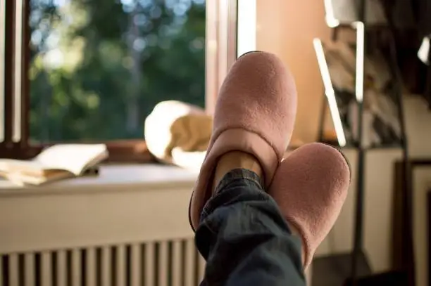 Relaxing at home - woman wearing jeans and pink slippers taking a break and looking at beautiful day through sunny window at home