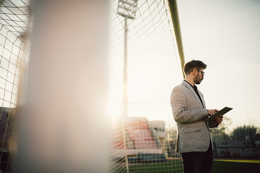 One man, standing on soccer field, using digital tablet.