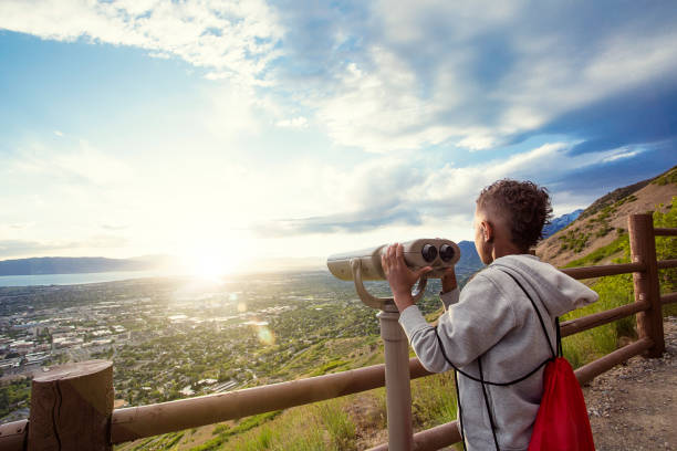 Looking out through binoculars at a beautiful mountain view Young boy looking out through binoculars at the mountain view of the city down below after hiking up a mountain trail. Lots of Copy spacec provo stock pictures, royalty-free photos & images